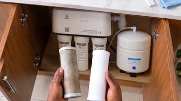  iClear technician inspecting filter cartridges under a kitchen sink in a Nigerian home